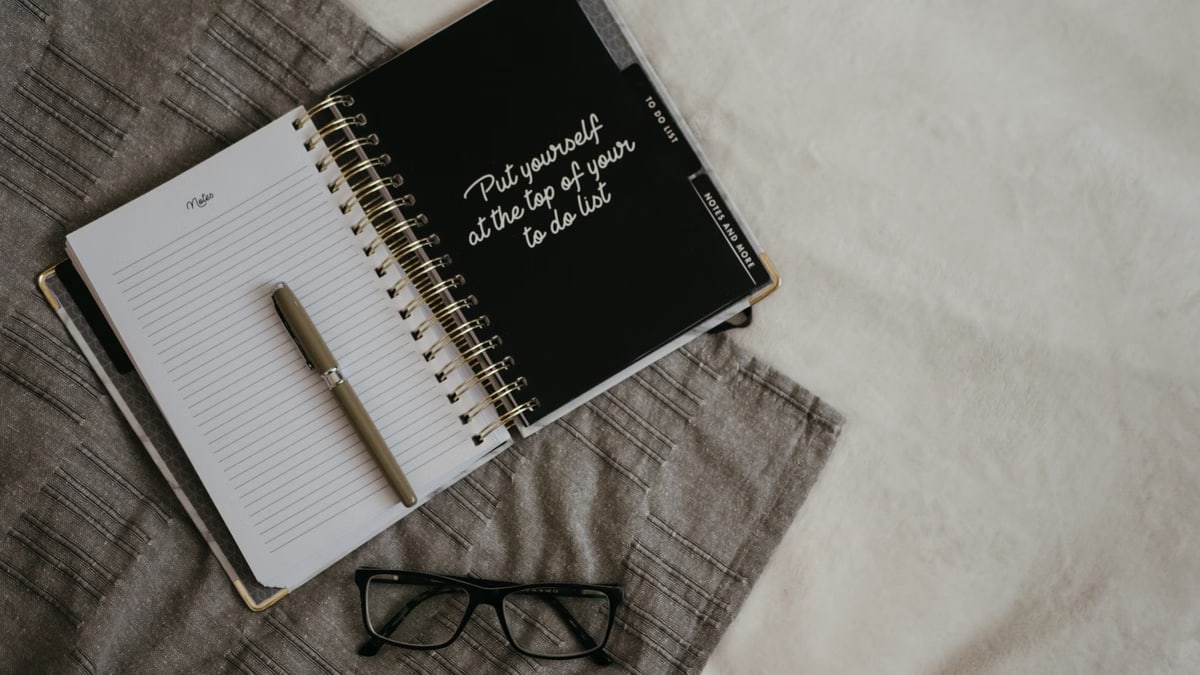 Stylish flatlay featuring a planner with quote, pen, and eyeglasses on a neutral background.